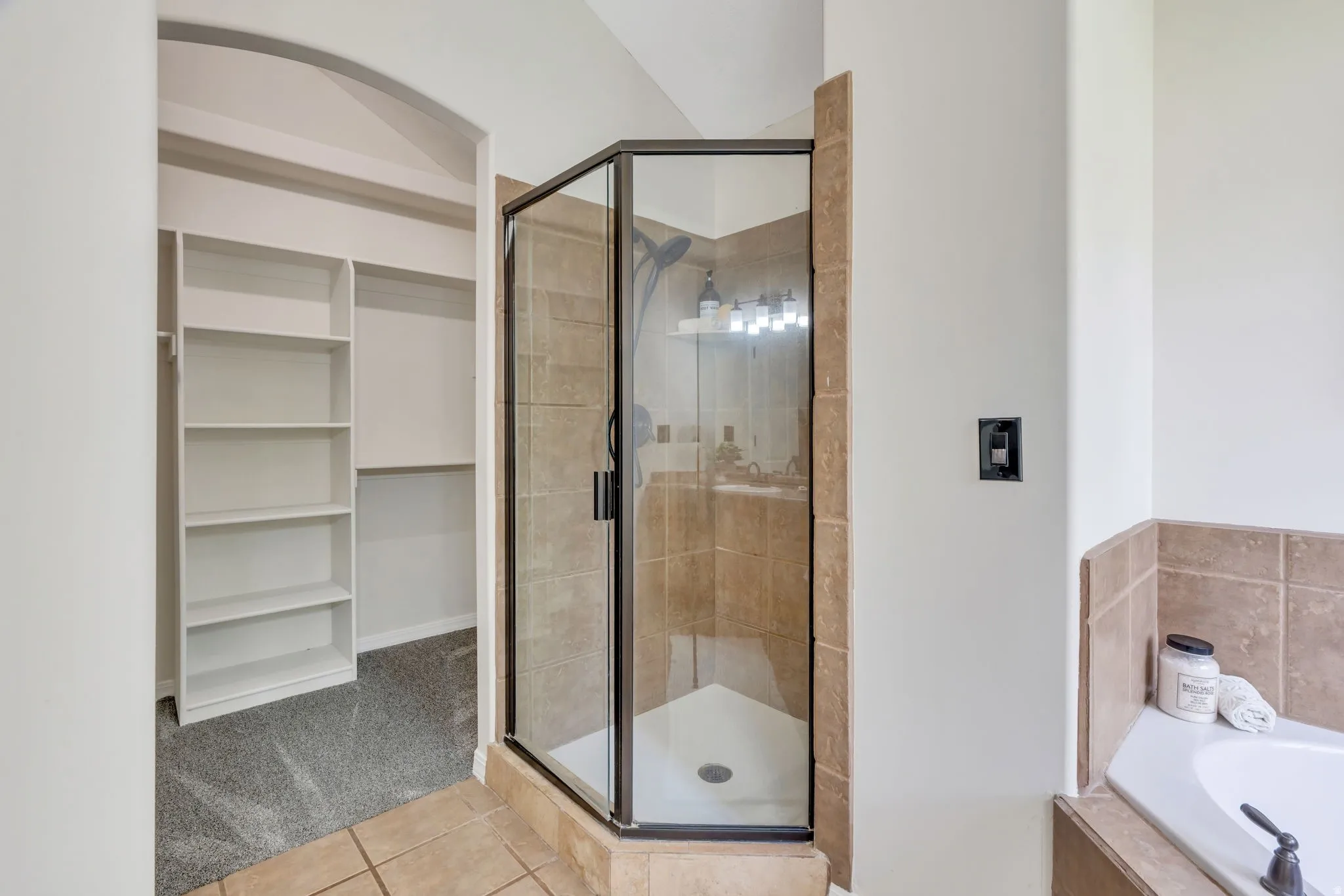 Glass-enclosed shower with tiled walls, built-in shelving, tiled flooring, and a built-in tub with tiled surround