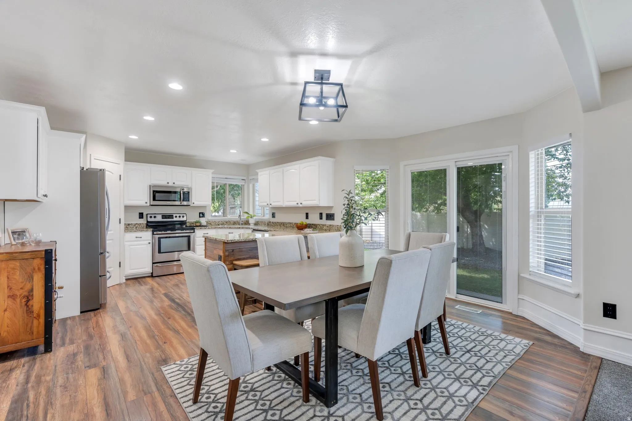 Wood-finish flooring throughout, white cabinetry with stainless steel appliances, recessed ceiling lights, a caged light fixture, and a sliding glass door