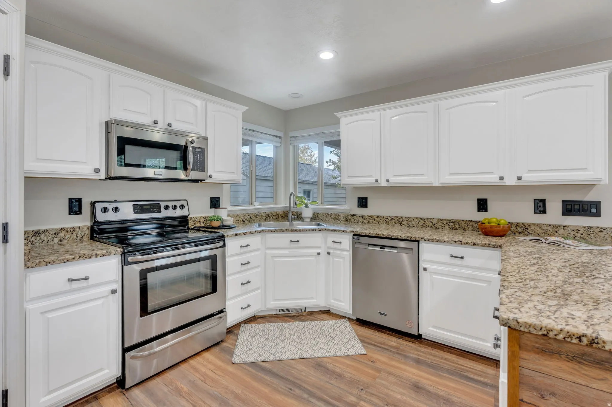 White cabinetry with dark hardware, stone-finish countertops, stainless steel appliances, wood-finish flooring, and recessed lighting