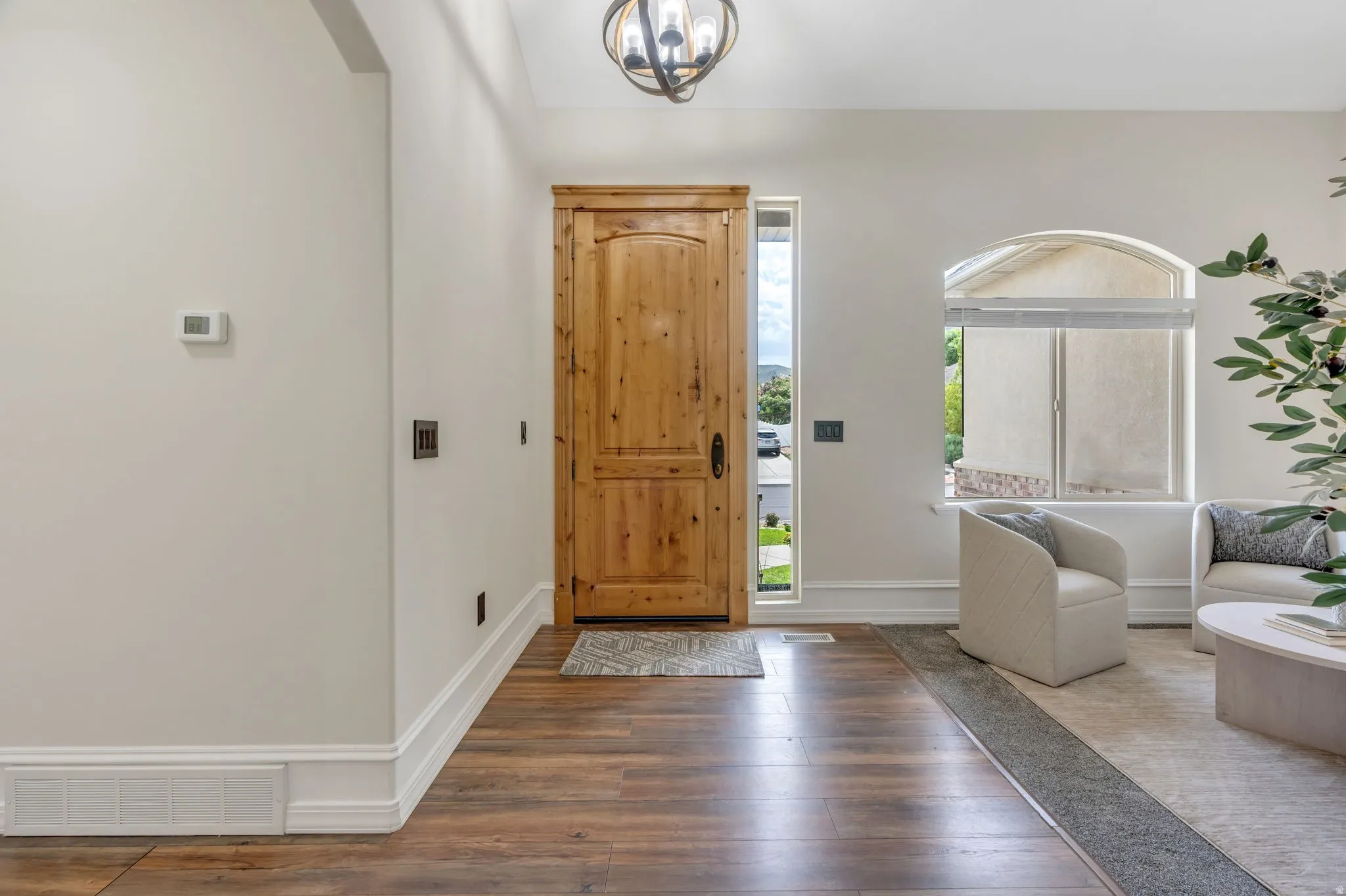 Wood-finish flooring, solid wood entry door, arched window, decorative ceiling light fixture, and white painted trim