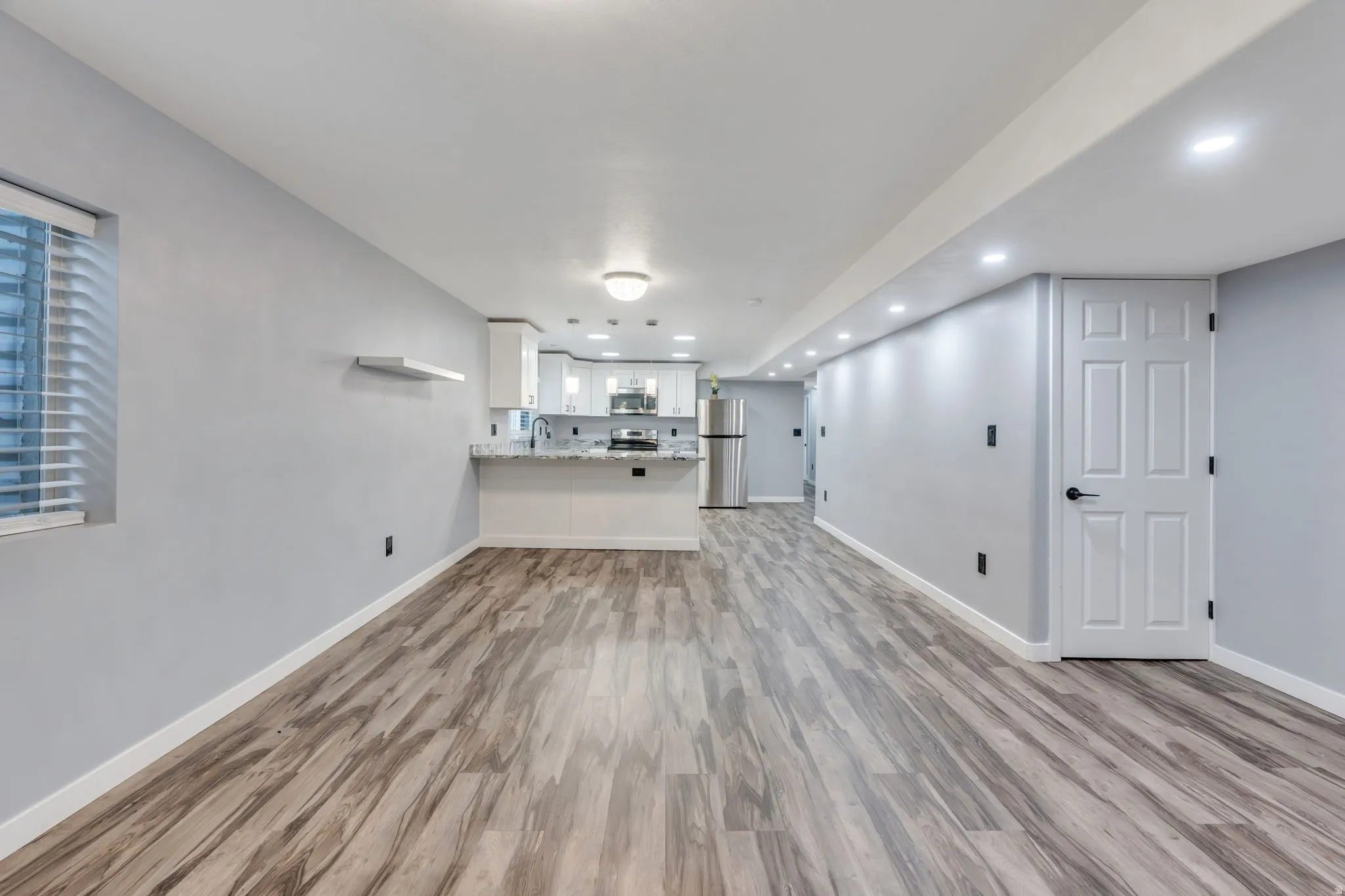 Spacious interior with wood-finish flooring, recessed lighting, and a kitchen featuring white cabinetry and stainless steel appliances