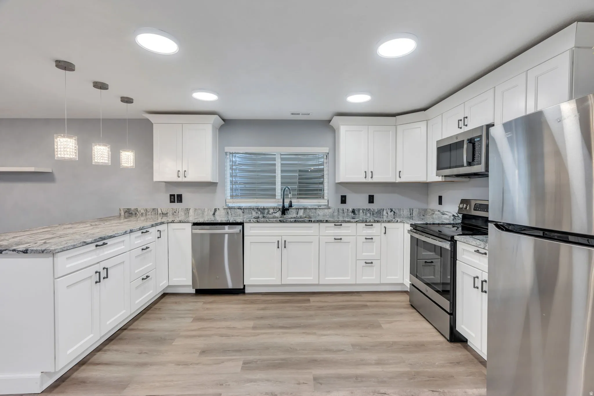 Kitchen featuring wood-finish flooring, white cabinetry, integrated stainless steel appliances, speckled stone countertops, and recessed lighting