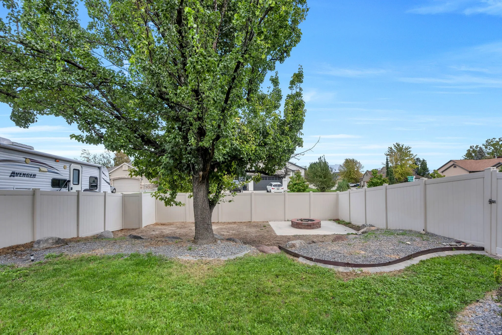 Expansive backyard featuring a mature tree, privacy fencing, concrete patio, and a built-in fire pit