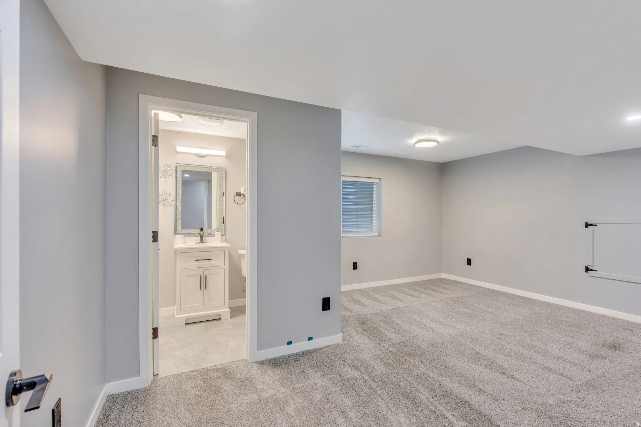 Spacious carpeted room with light grey walls and a window featuring horizontal blinds