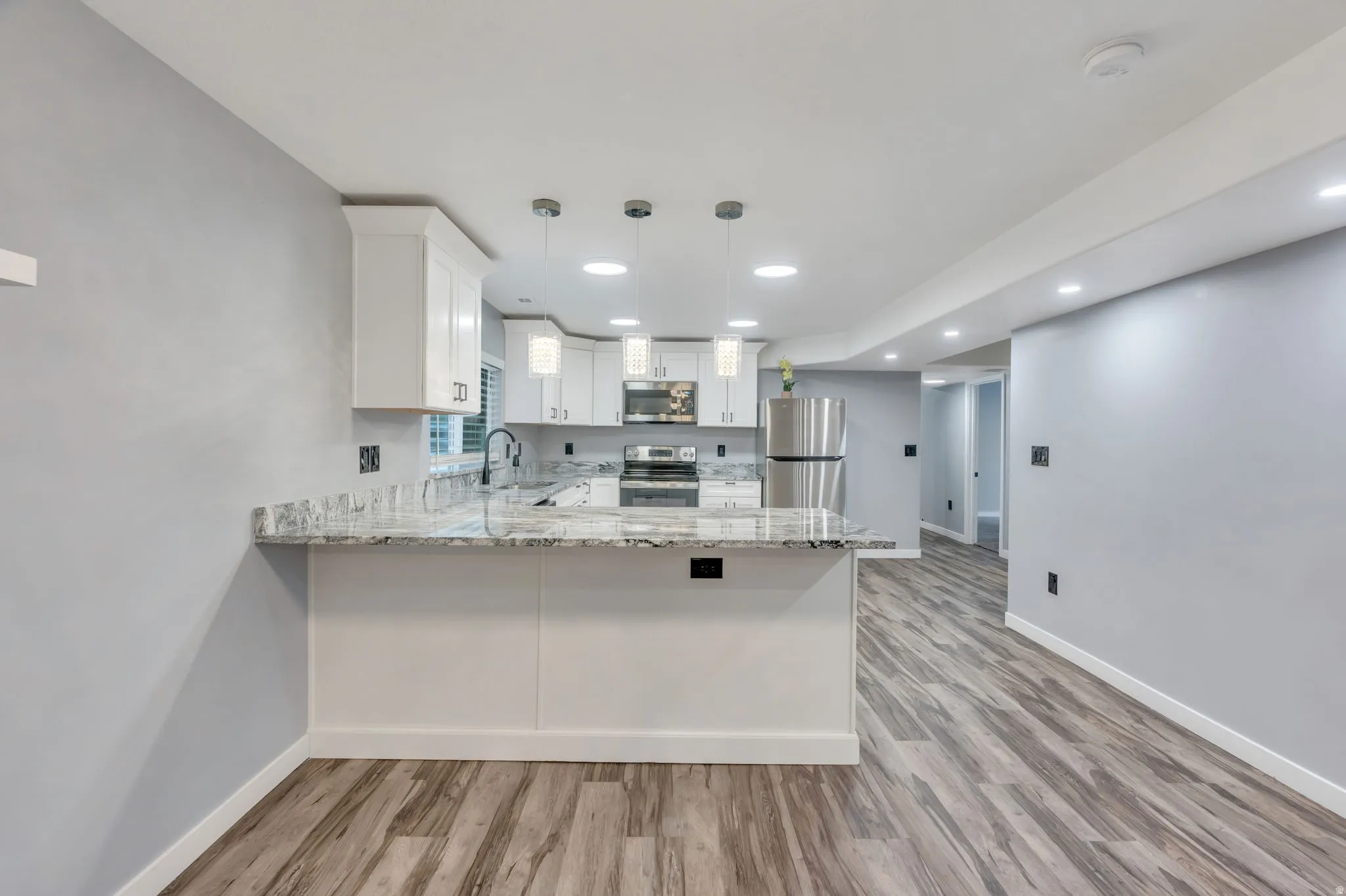 Contemporary kitchen featuring white cabinetry, a stone-finish countertop, stainless steel appliances, and pendant lighting