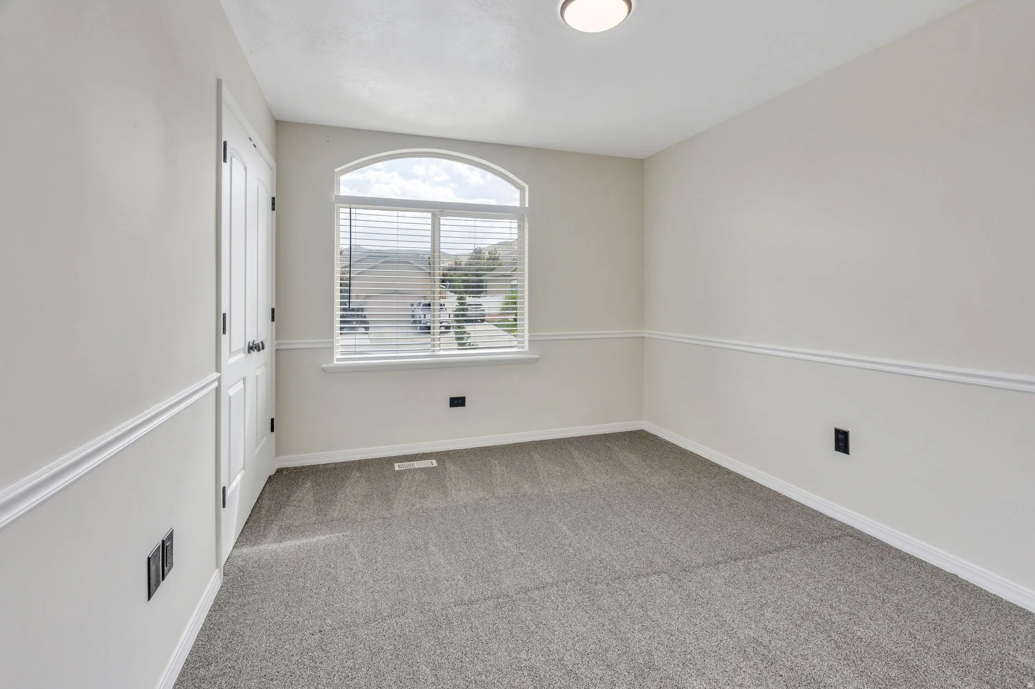 Arched window with horizontal blinds, carpeted flooring, two-panel interior door, and wall molding