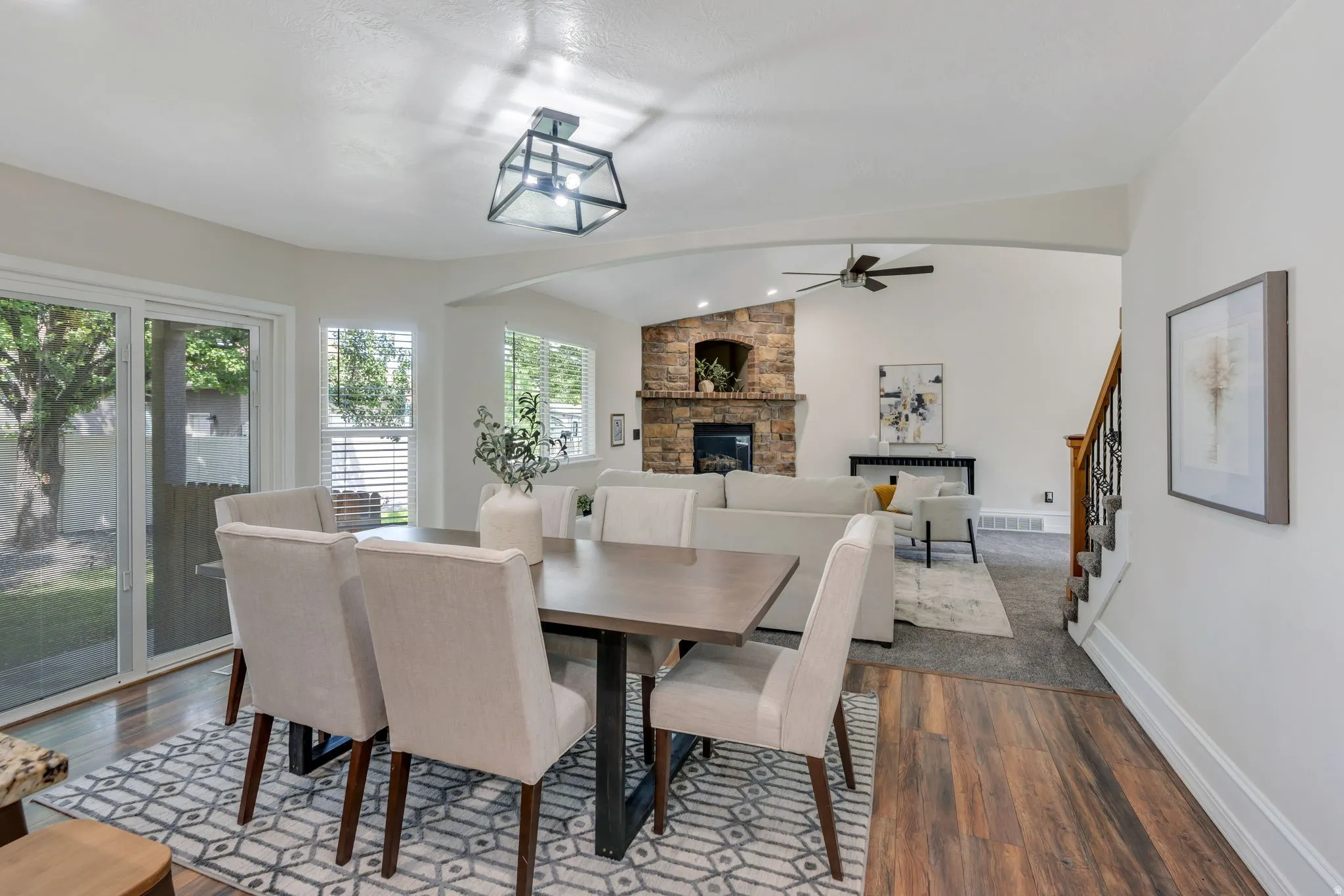 Wood-finish flooring, glass sliding door, stone fireplace, vaulted ceiling, and staircase with wrought iron balusters