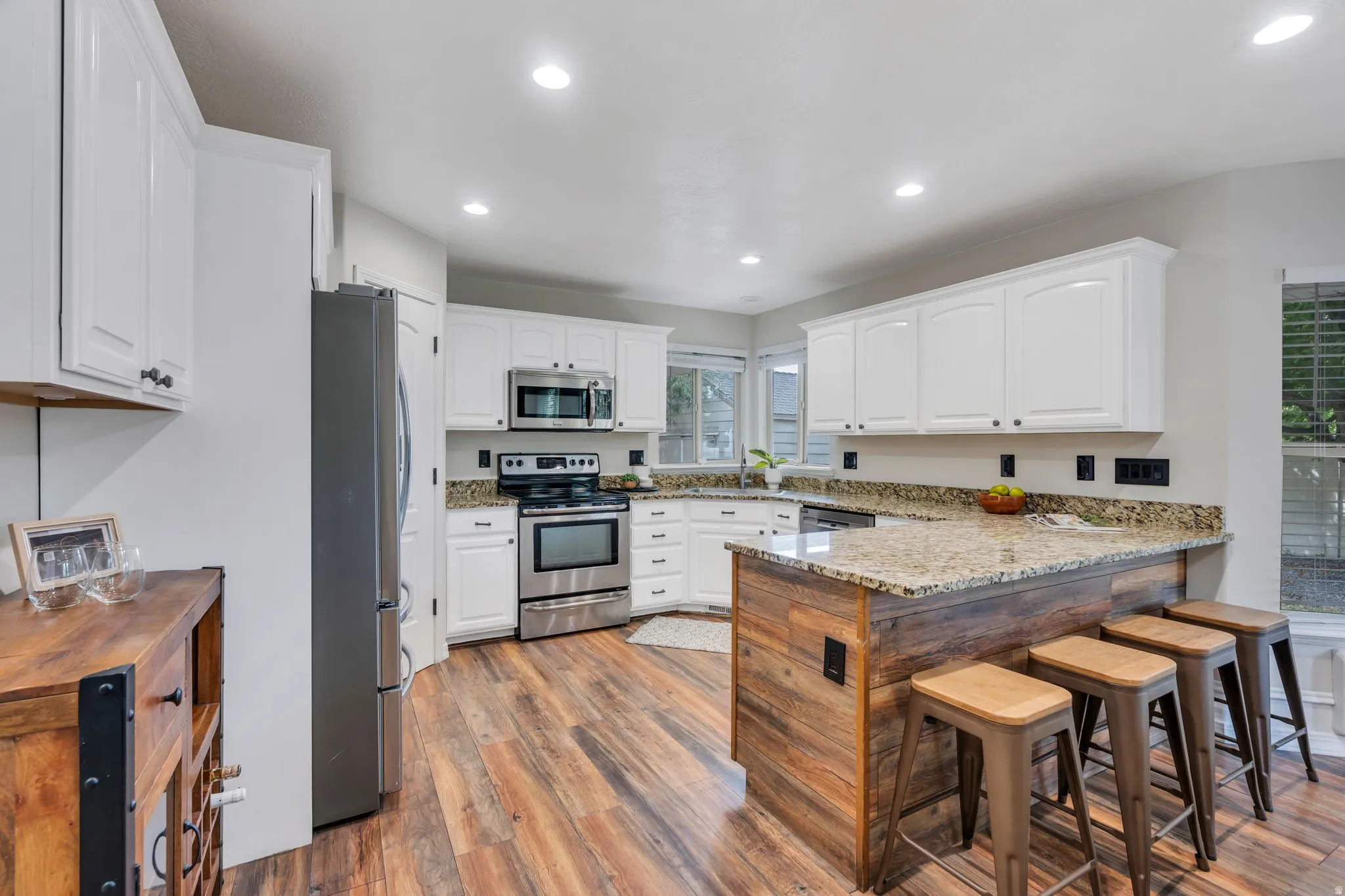 Kitchen featuring wood-finish flooring, white cabinetry, granite countertops, stainless steel appliances, and recessed lighting