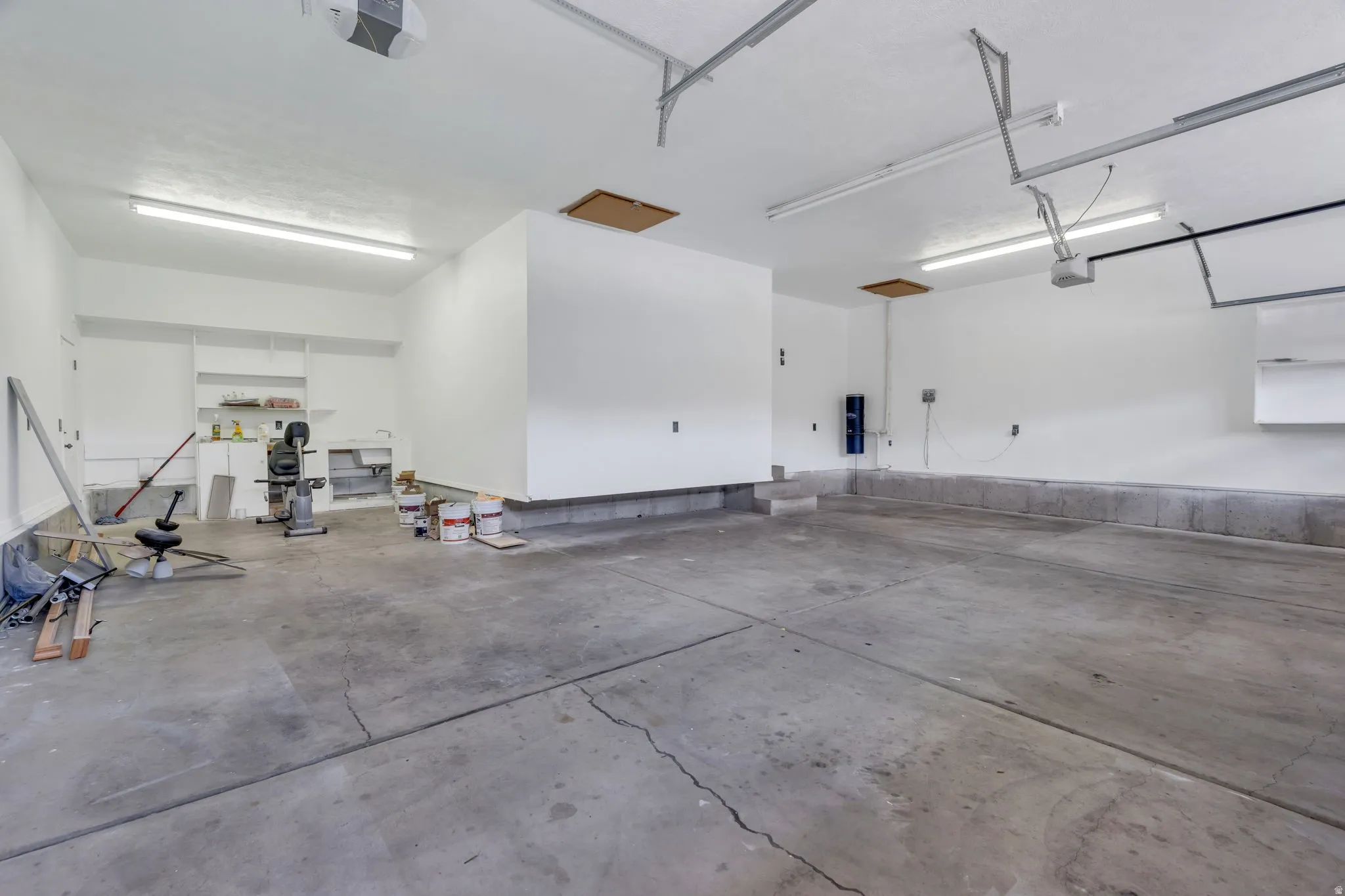 Spacious concrete-floor garage featuring built-in shelving, overhead lighting, and built-in utility sink