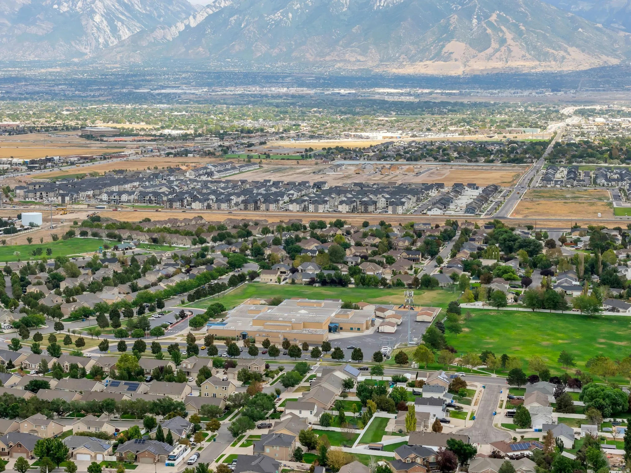 Expansive suburban landscape with varied residential developments, verdant green spaces, and a mountainous backdrop