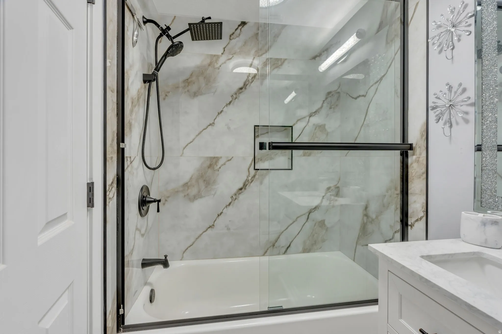 Bathtub with a glass shower enclosure, a rain shower head, and a handheld shower head