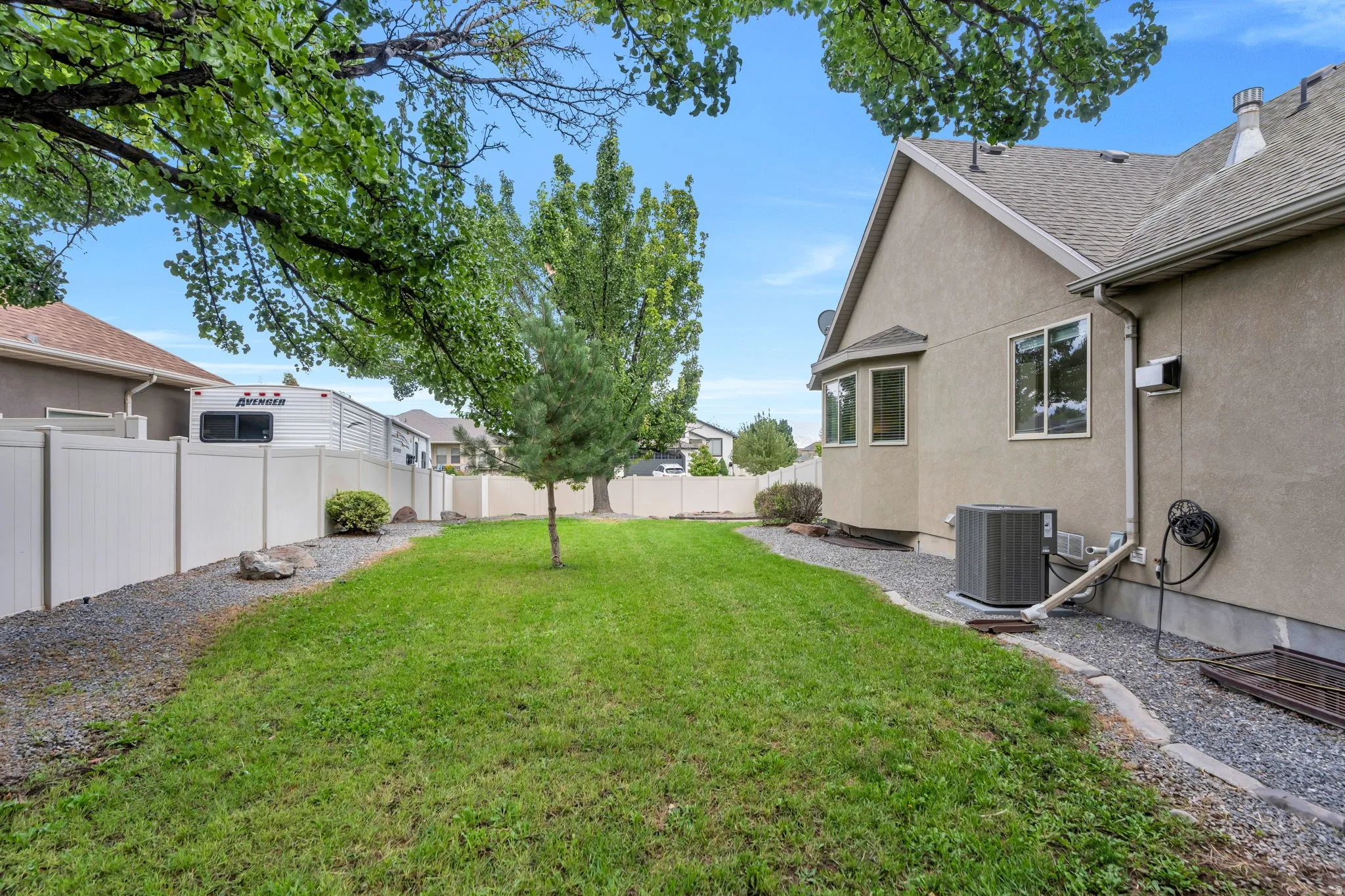 Expansive backyard featuring a green lawn, established trees, and a white privacy fence