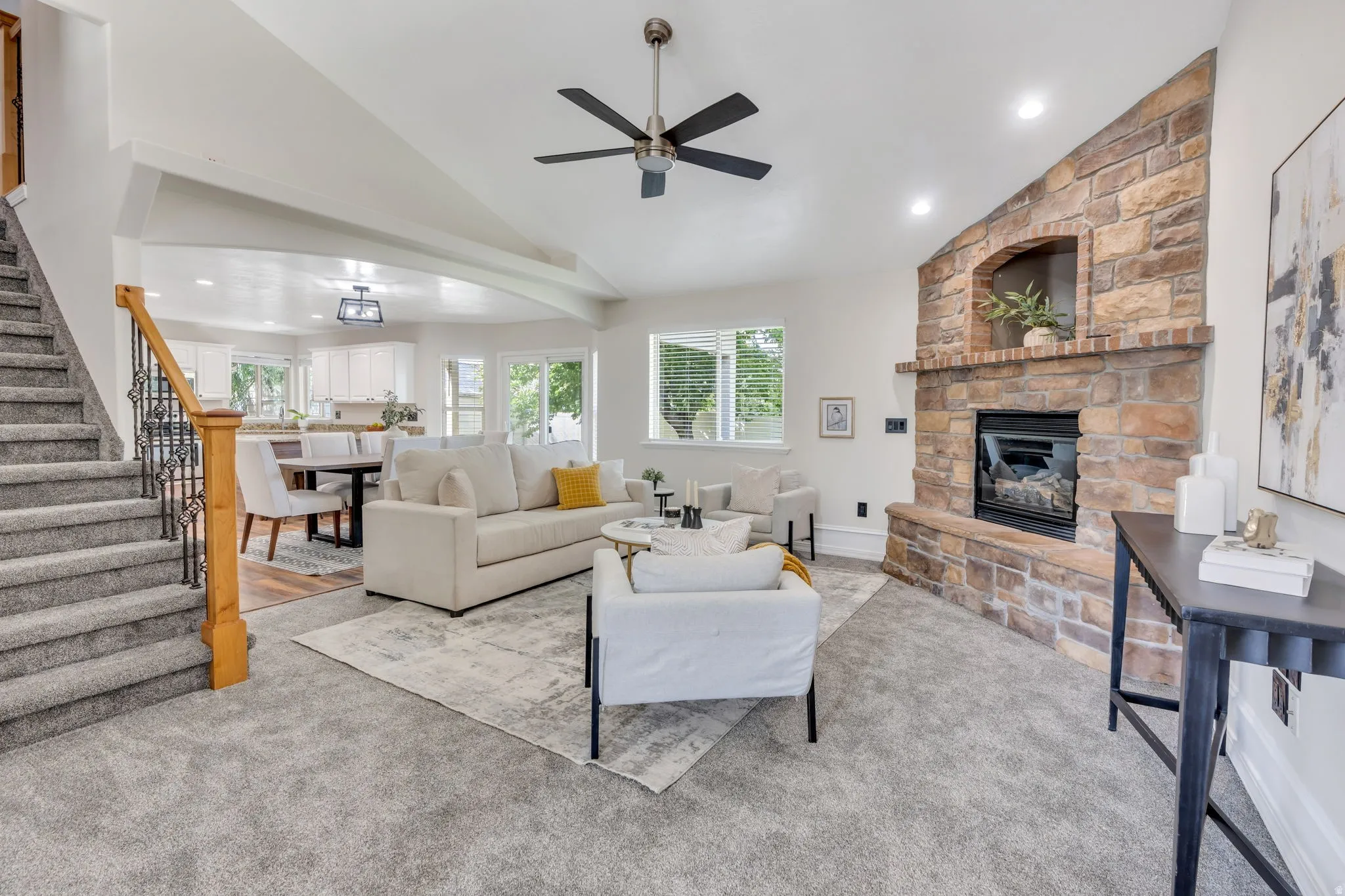 Stone-faced fireplace with hearth, vaulted ceiling, recessed lighting, ceiling fan, and carpeted flooring