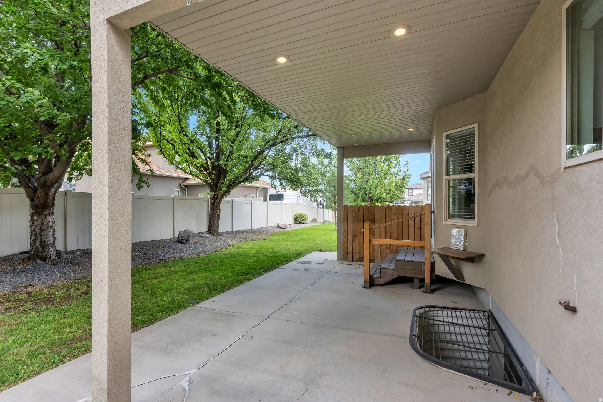 Covered concrete patio with recessed lighting, bordered by a manicured lawn and privacy fencing