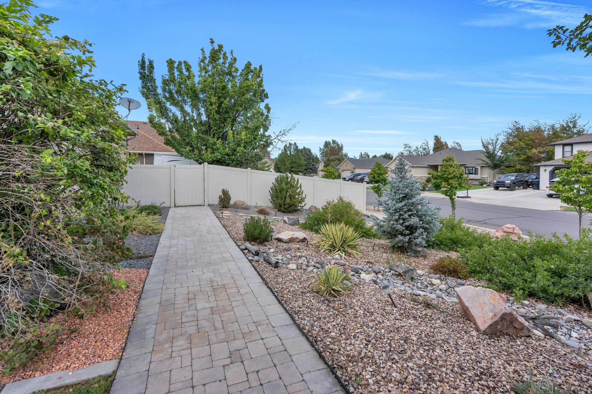 Paver pathway leading to a gated privacy fence, bordered by low-maintenance landscaping with decorative rocks and varied plant types