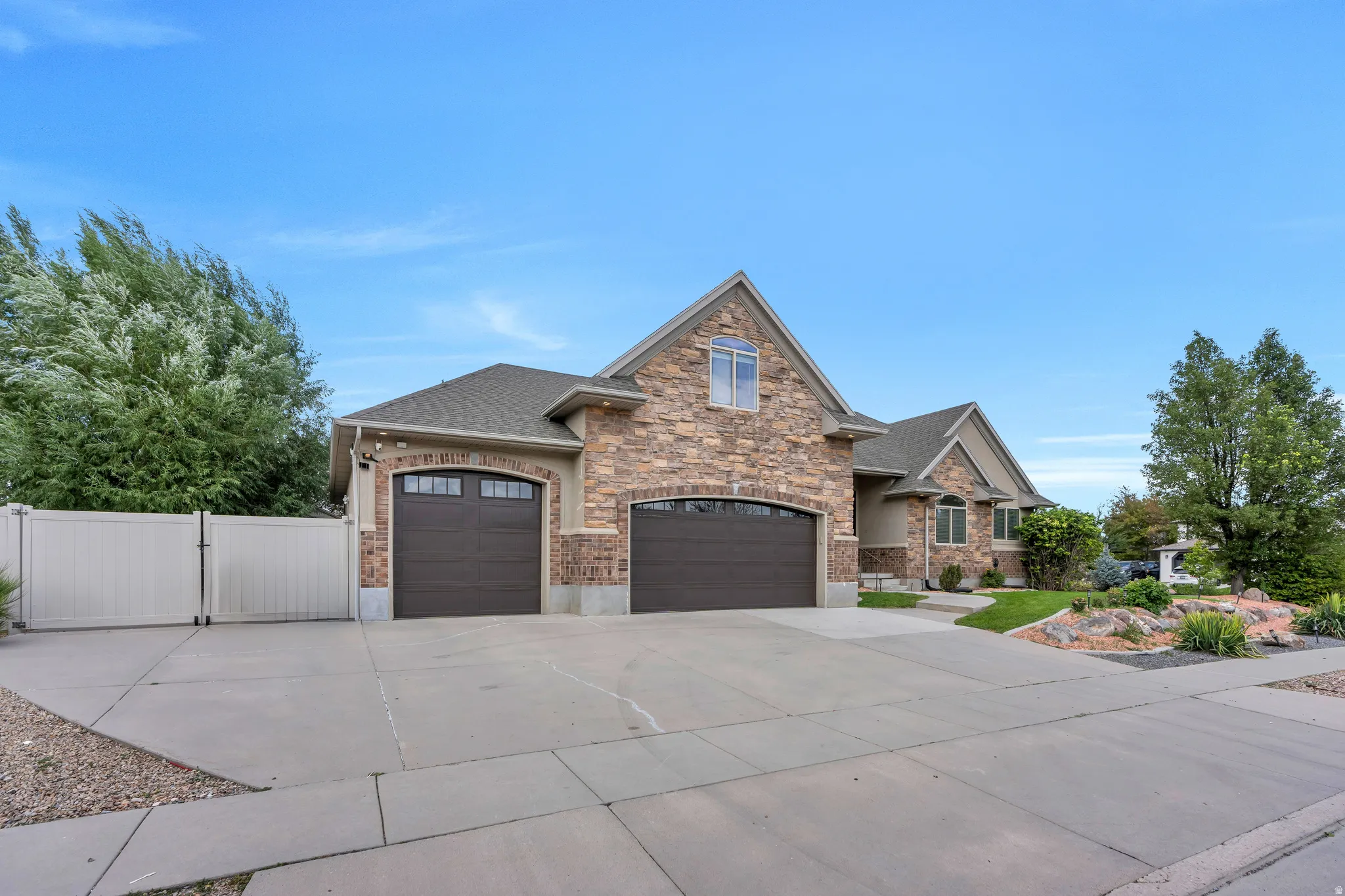 Stone and stucco exterior with an arched garage entry, concrete driveway, and mature landscaping
