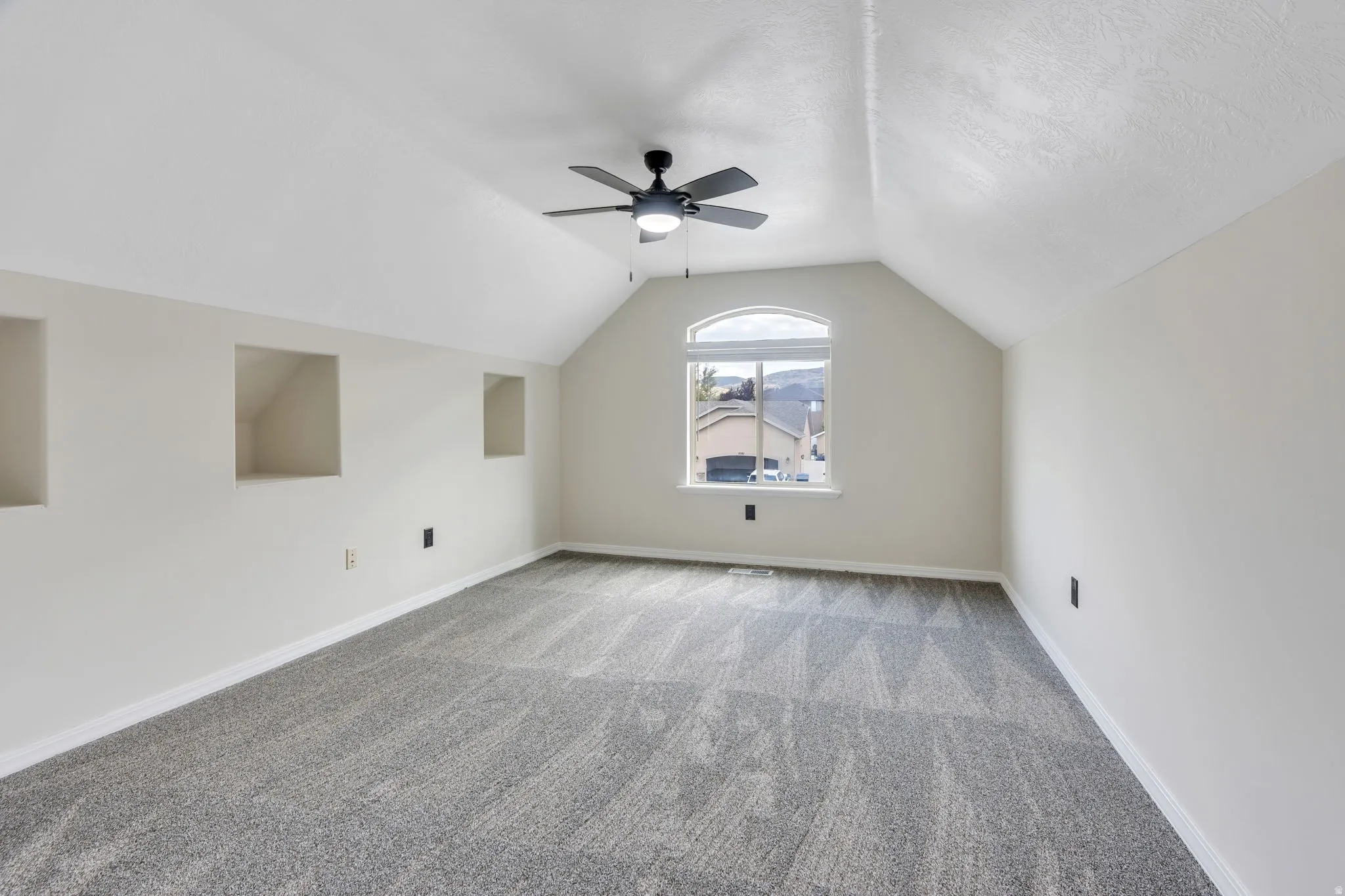 Vaulted ceiling with a ceiling fan, arched window, built-in wall niches, and neutral carpeting