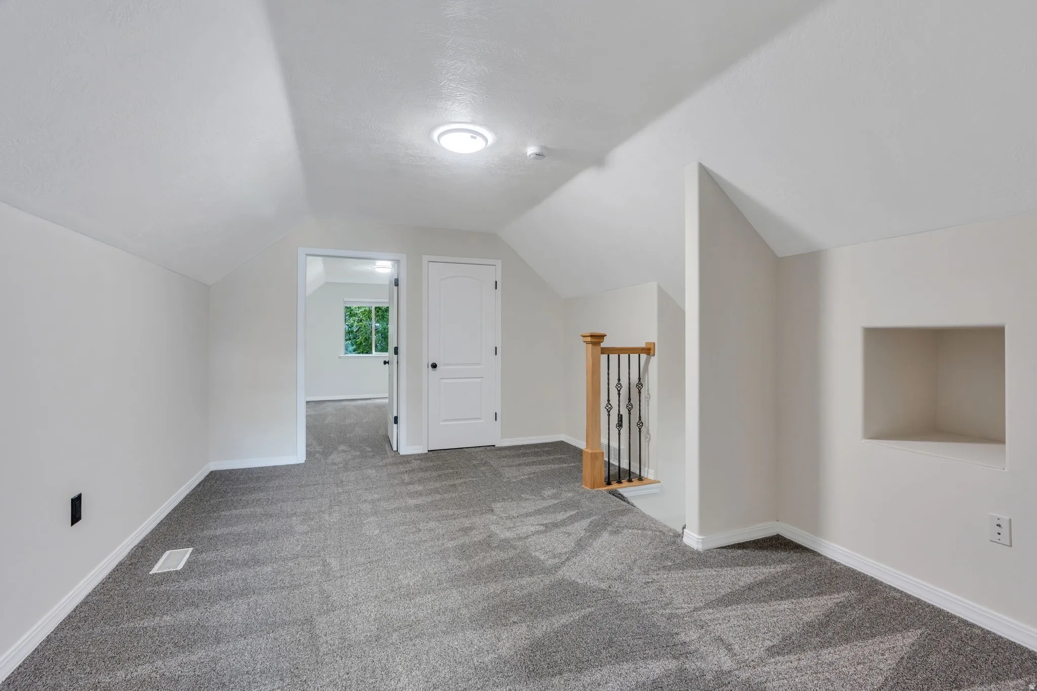 Carpeted room with a built-in wall niche, recessed lighting, and a wooden stair railing with wrought iron balusters