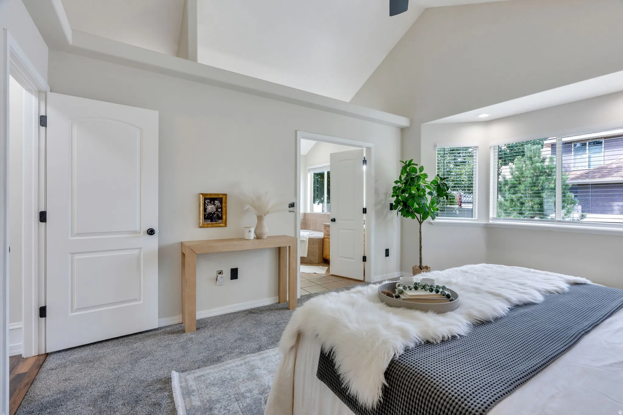 Vaulted ceiling with exposed beams, bay window, light gray carpeting, neutral wall finishes, and a paneled door
