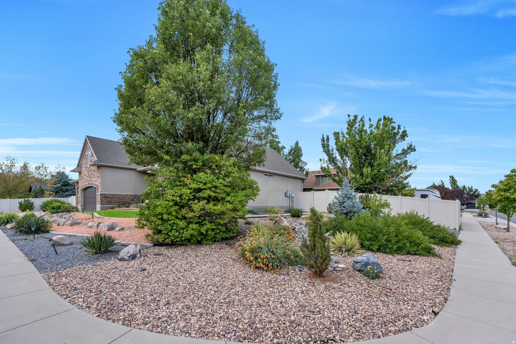 Stone and stucco exterior with an arched garage door, mature trees, and a gravel and rock landscaping
