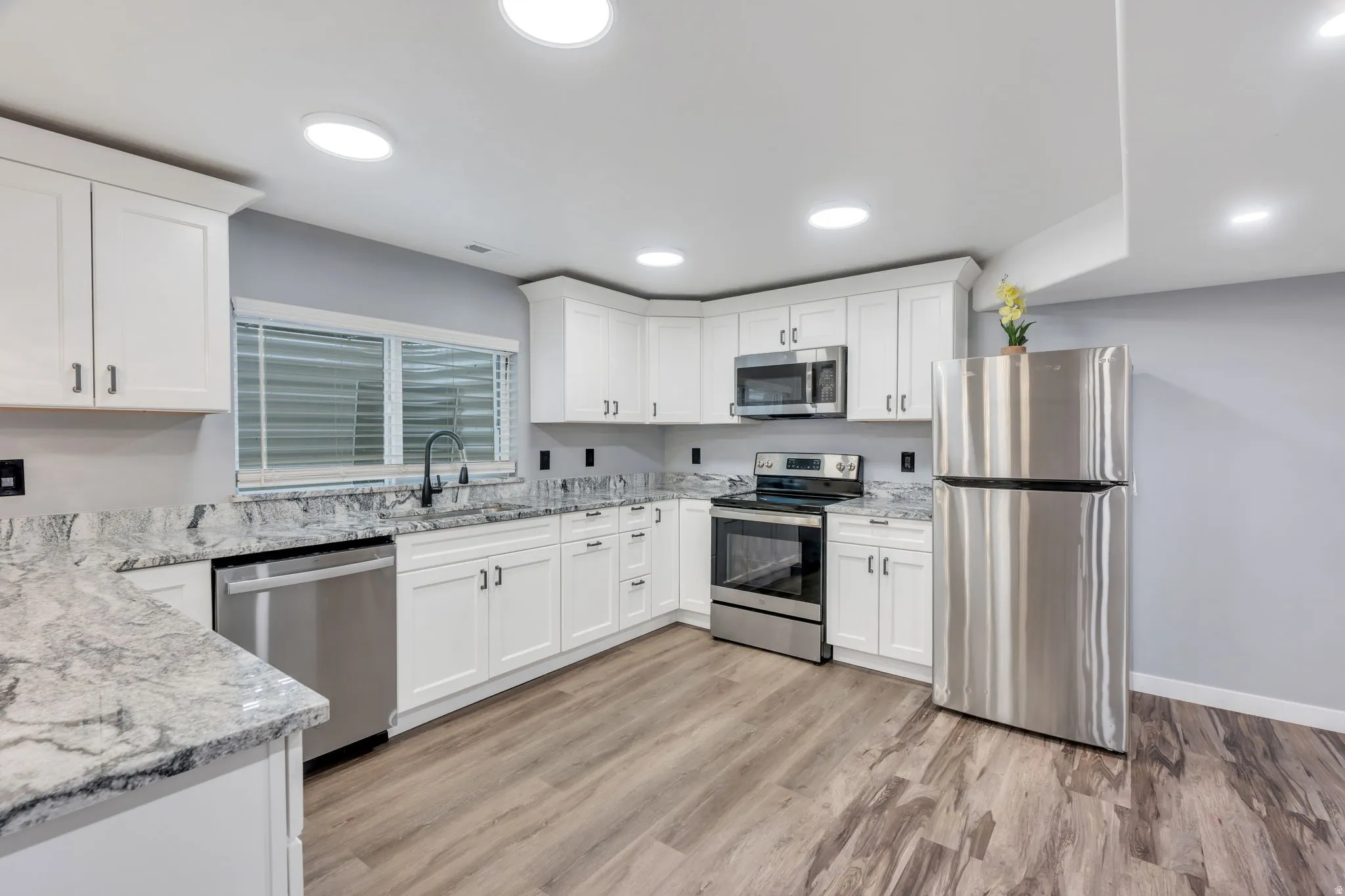 Kitchen featuring white cabinetry, stainless steel appliances, speckled countertops, wood-finish flooring, and recessed lighting