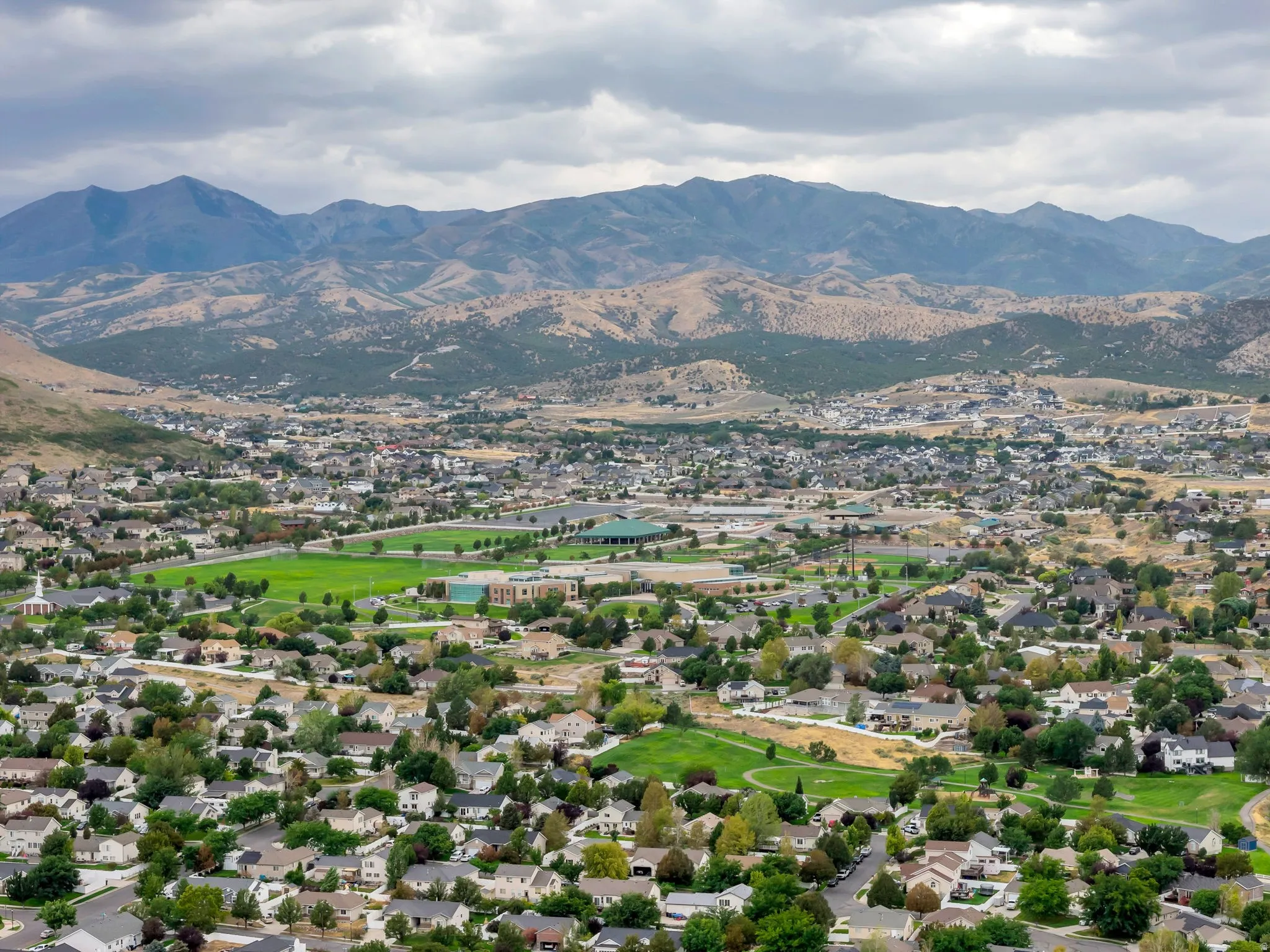 Expansive residential area with a prominent mountain backdrop, featuring numerous single-family homes, verdant green spaces, and mature trees