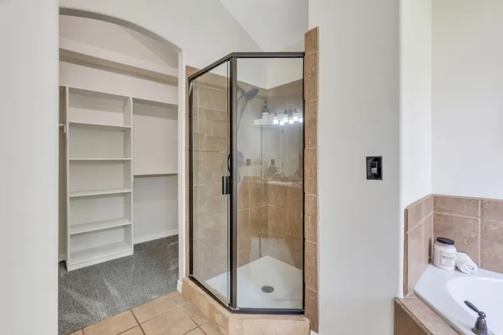 Glass-enclosed shower with tiled walls, built-in shelving, tiled flooring, and a built-in tub with tiled surround