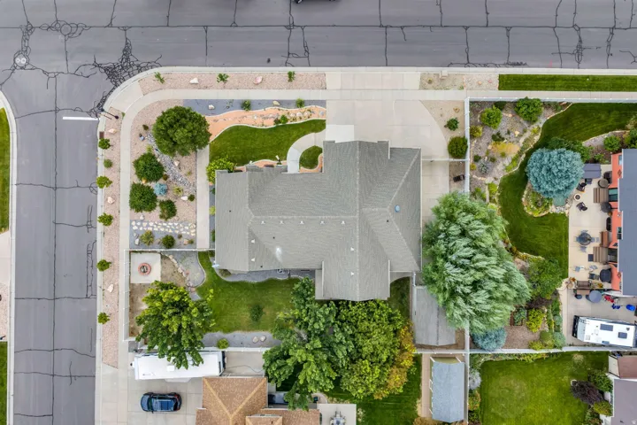 Aerial view showcasing a residence with a generous flat roof, mature landscaping throughout the grounds, and defined hardscaped pathways