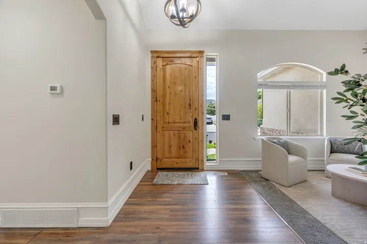 Wood-finish flooring, solid wood entry door, arched window, decorative ceiling light fixture, and white painted trim
