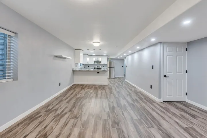 Spacious interior with wood-finish flooring, recessed lighting, and a kitchen featuring white cabinetry and stainless steel appliances