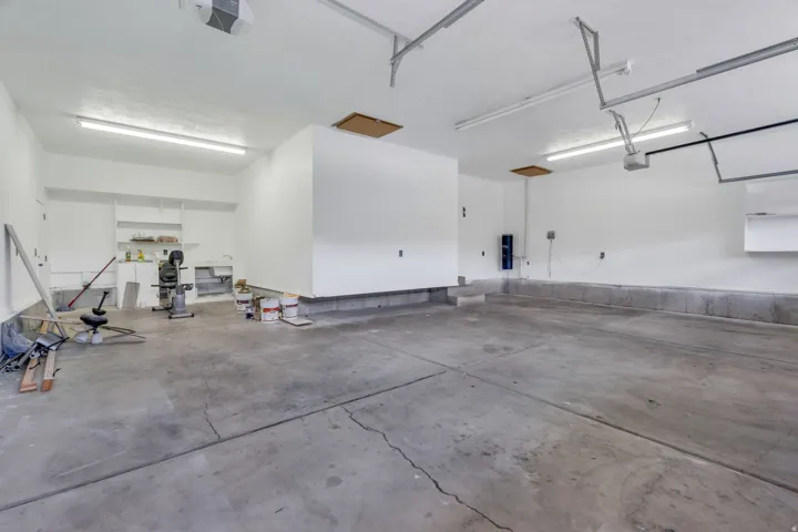 Spacious concrete-floor garage featuring built-in shelving, overhead lighting, and built-in utility sink
