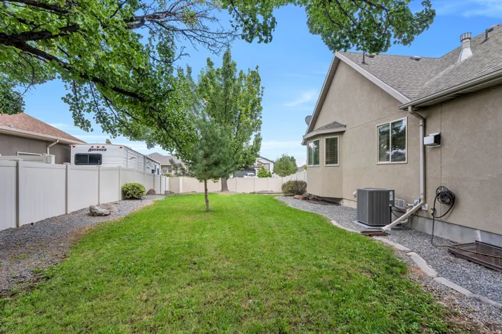Expansive backyard featuring a green lawn, established trees, and a white privacy fence