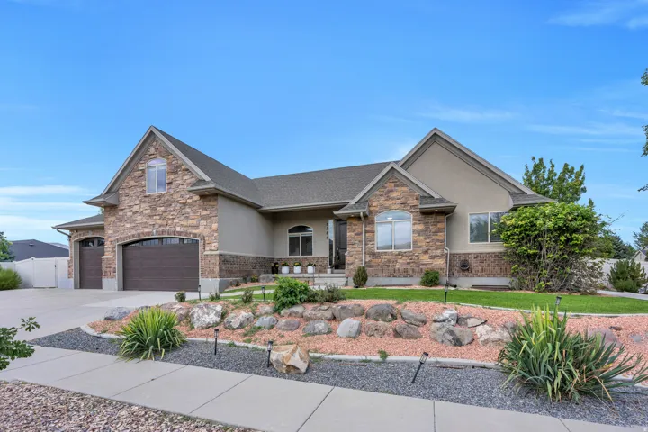 Stone and stucco exterior, arched garage doors, established landscaping with rock features, concrete driveway, and a paved walkway