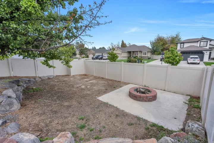 Enclosed backyard featuring a fire pit on a concrete pad, a rock border, and a privacy fence