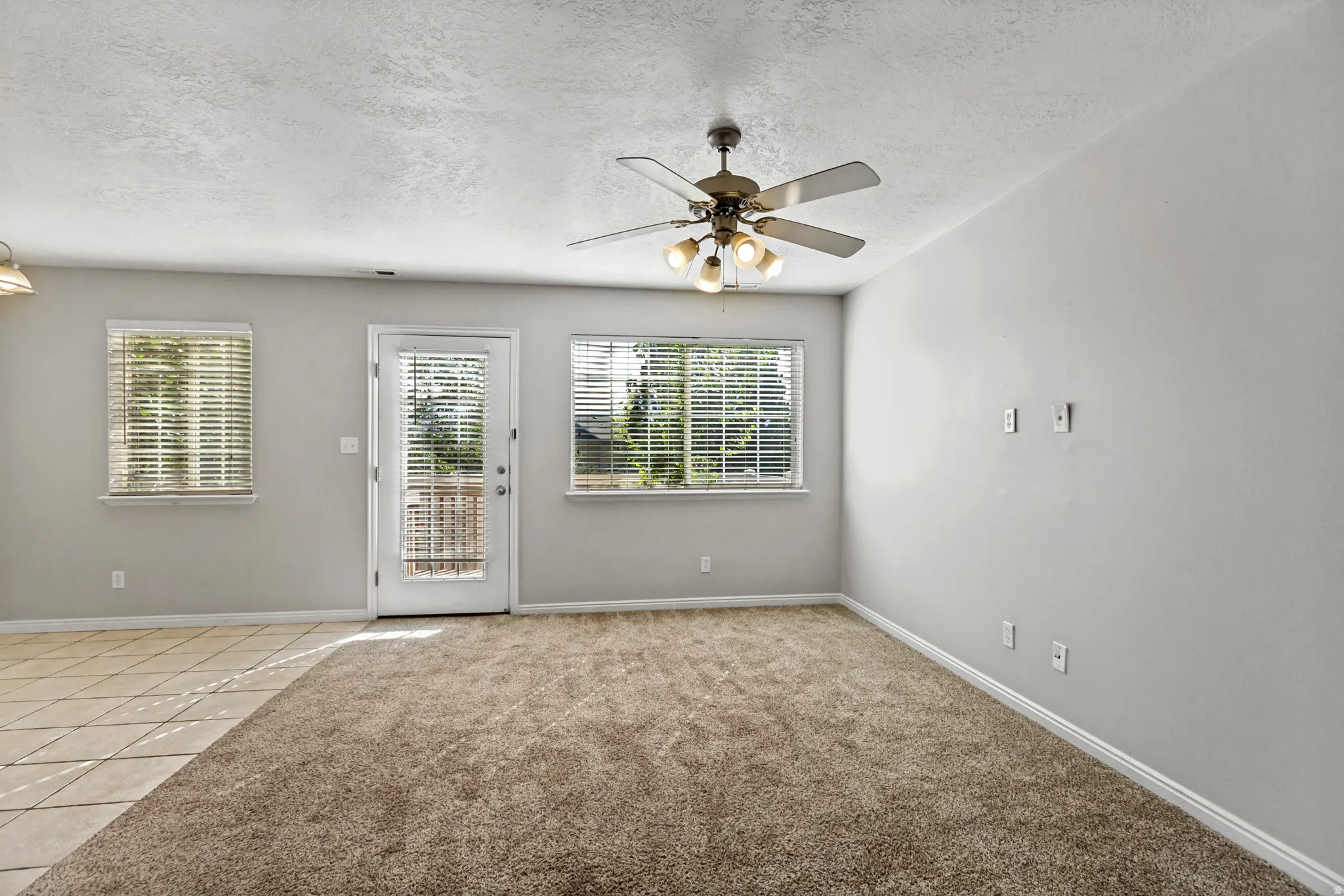 Spacious room featuring neutral carpeting, a ceiling fan with integrated lighting, a glass-paned exterior door, and two windows with blinds