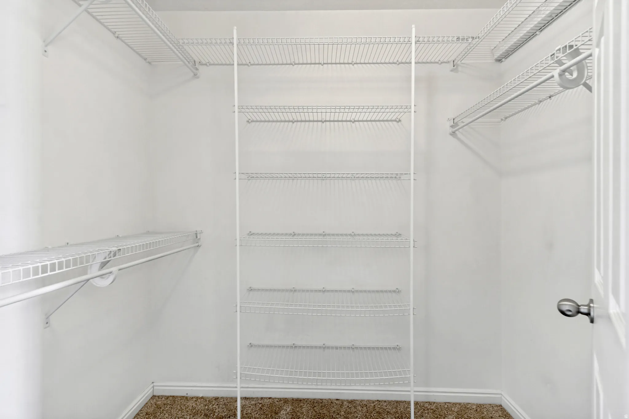White wire shelving system, multiple storage shelves, hanging rods, light-colored walls, brown carpet flooring