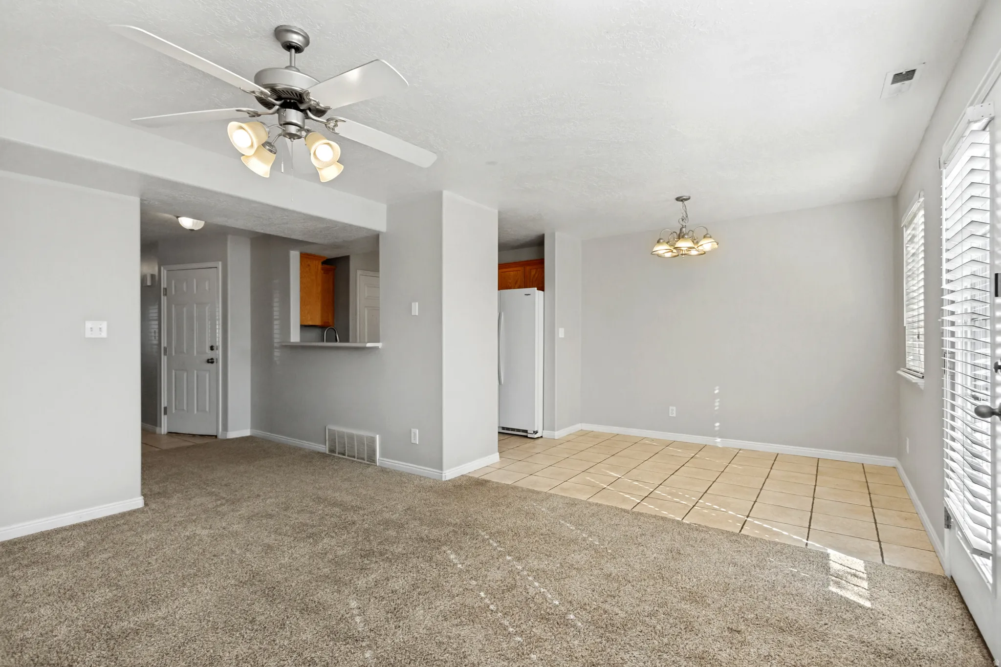 Carpeted living area, tile flooring in dining area, ceiling fan with integrated lighting, chandelier, and white paneled entry door