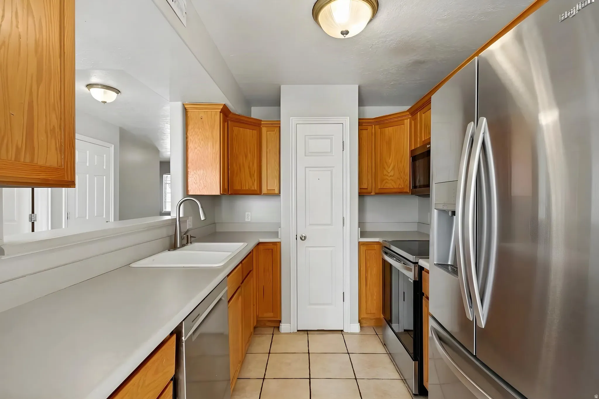 Kitchen featuring wood-finish cabinetry, stainless steel appliances, a double basin sink, and tile flooring