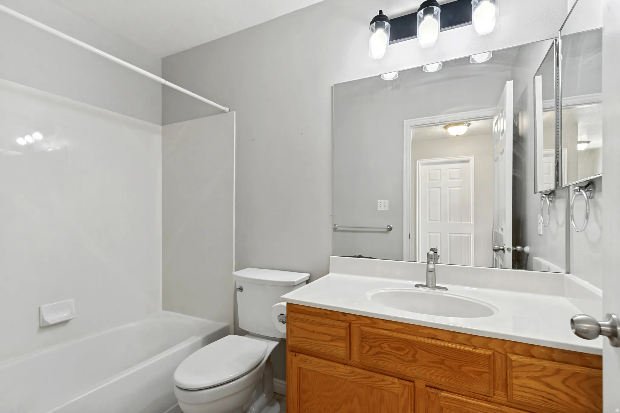 White bathtub with integrated shower, single-sink vanity with wood-finish cabinetry, and overhead light fixture