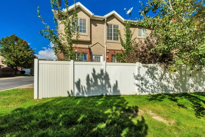 Two-story stucco and brick exterior featuring a white privacy fence and established trees