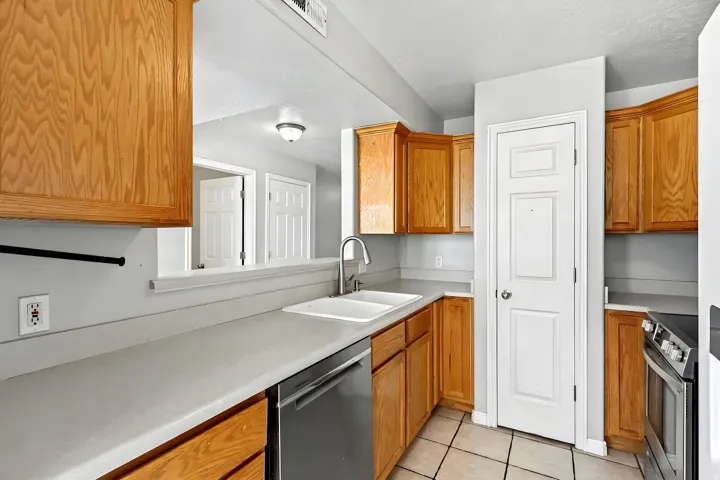 Kitchen featuring wood cabinetry, light-toned countertops, a dual basin sink with a gooseneck faucet, a stainless steel dishwasher, and tile flooring