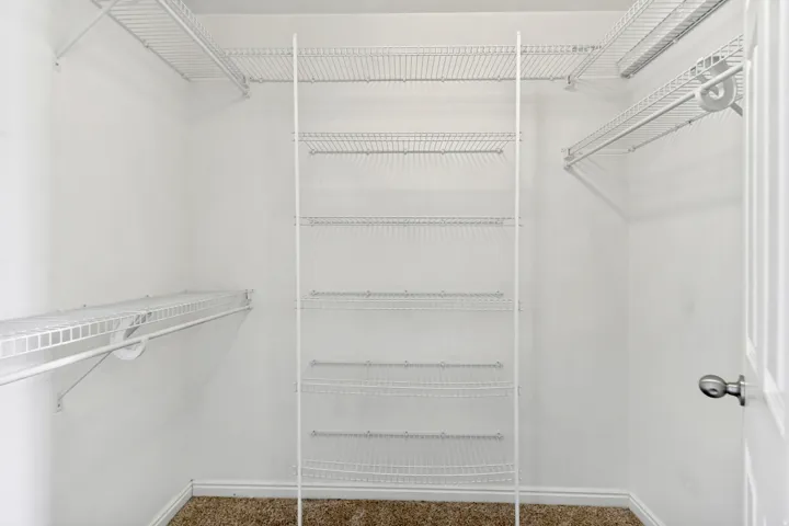 White wire shelving system, multiple storage shelves, hanging rods, light-colored walls, brown carpet flooring