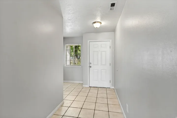 Foyer with square tile flooring, a paneled entry door, a flush-mount light fixture, and a window with horizontal blinds