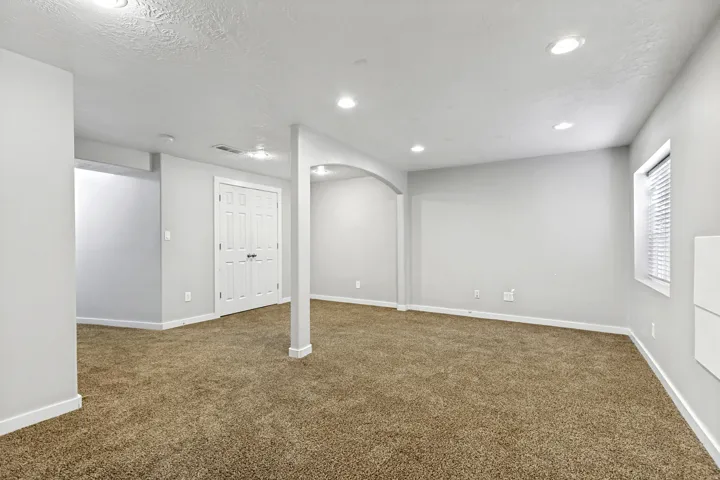 Expansive room with brown carpet flooring, recessed lighting, and a white paneled door