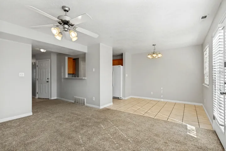 Carpeted living area, tile flooring in dining area, ceiling fan with integrated lighting, chandelier, and white paneled entry door