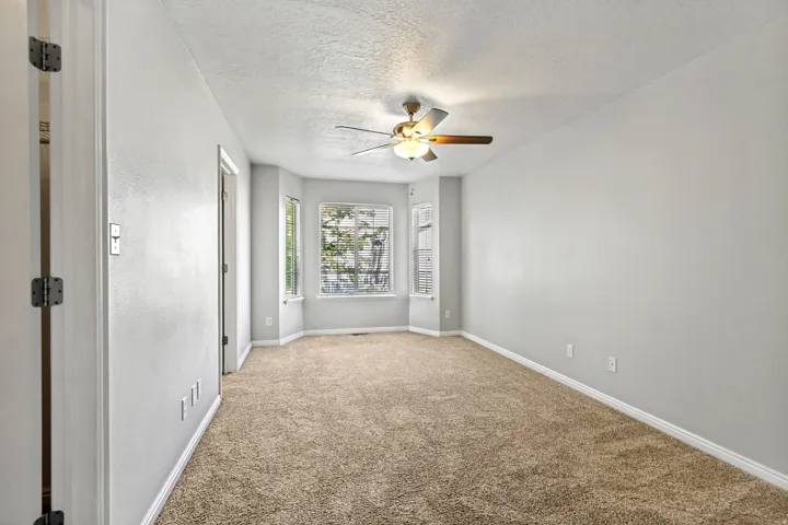 Recessed bay windows with white trim, ceiling fan with light fixture, light gray walls, and textured carpet flooring