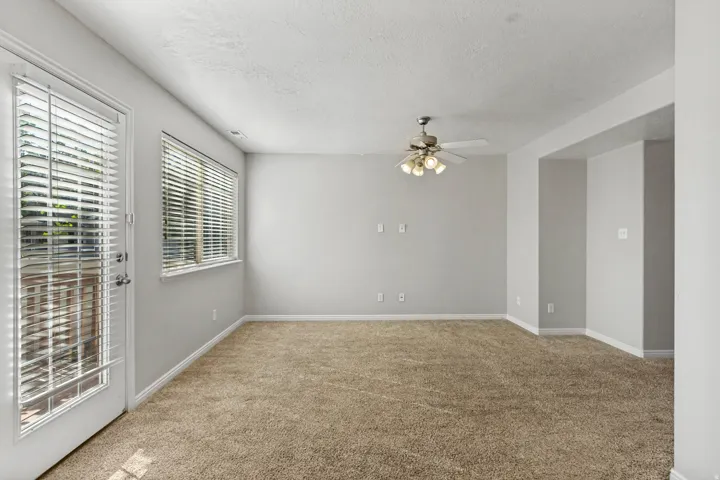 Neutral wall paint, light-colored carpeting, a ceiling fan with integrated lighting, a window with blinds, and a glass-paneled door