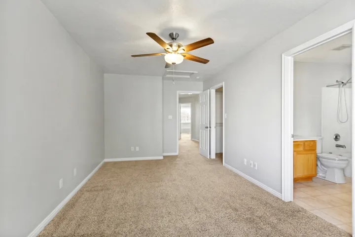 Carpeted flooring, neutral wall tones, ceiling fan with integrated lighting, white interior doors, and a bathroom with a shower and wood-finish vanity