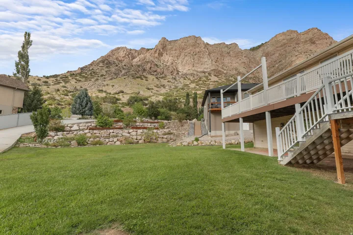 Expansive manicured lawn with mature landscaping and stone retaining wall, backed by dramatic mountain terrain