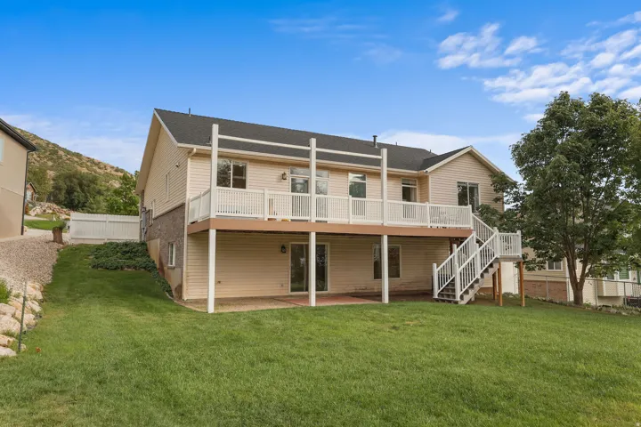 Expansive backyard featuring a manicured lawn, a large upper-level deck with white railings, a lower-level patio, and a staircase providing direct access to the yard